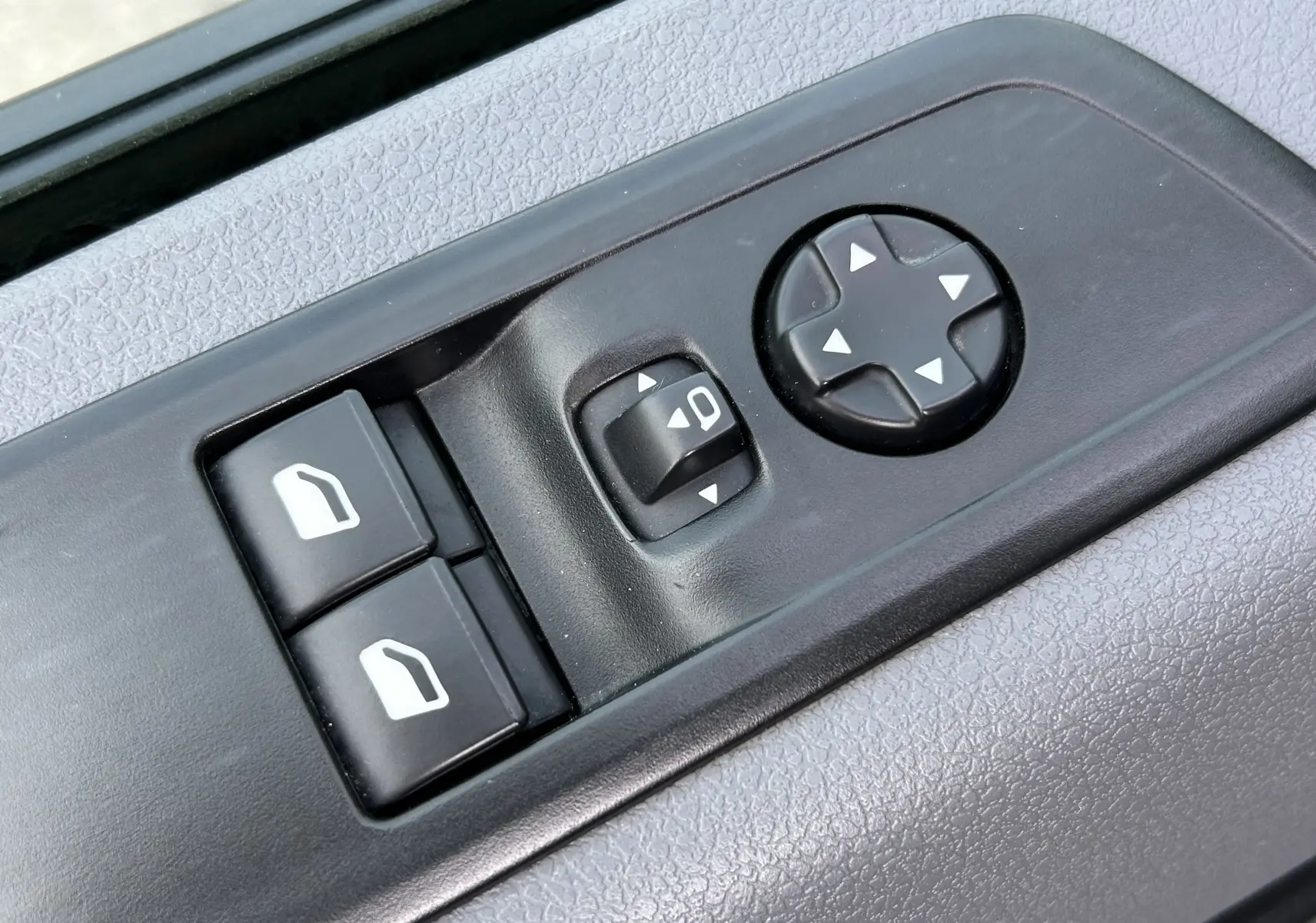 Gros plan sur les commandes de réglage des vitres et des rétroviseurs côté conducteur d’un Opel Vivaro Combi noir.