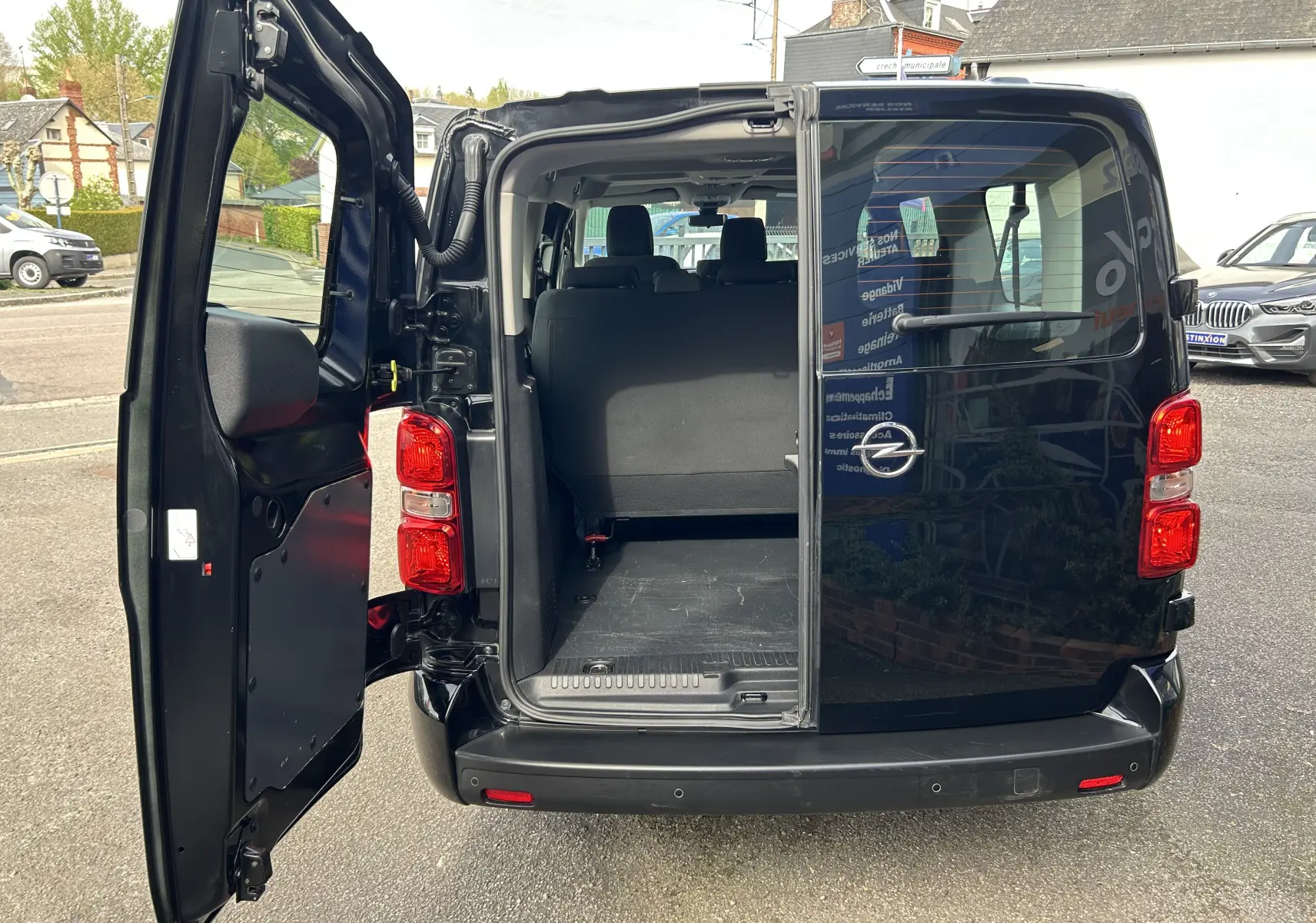 Vue arrière d'un Opel Vivaro Combi noir 2022 avec porte battante gauche ouverte montrant l'espace de chargement.