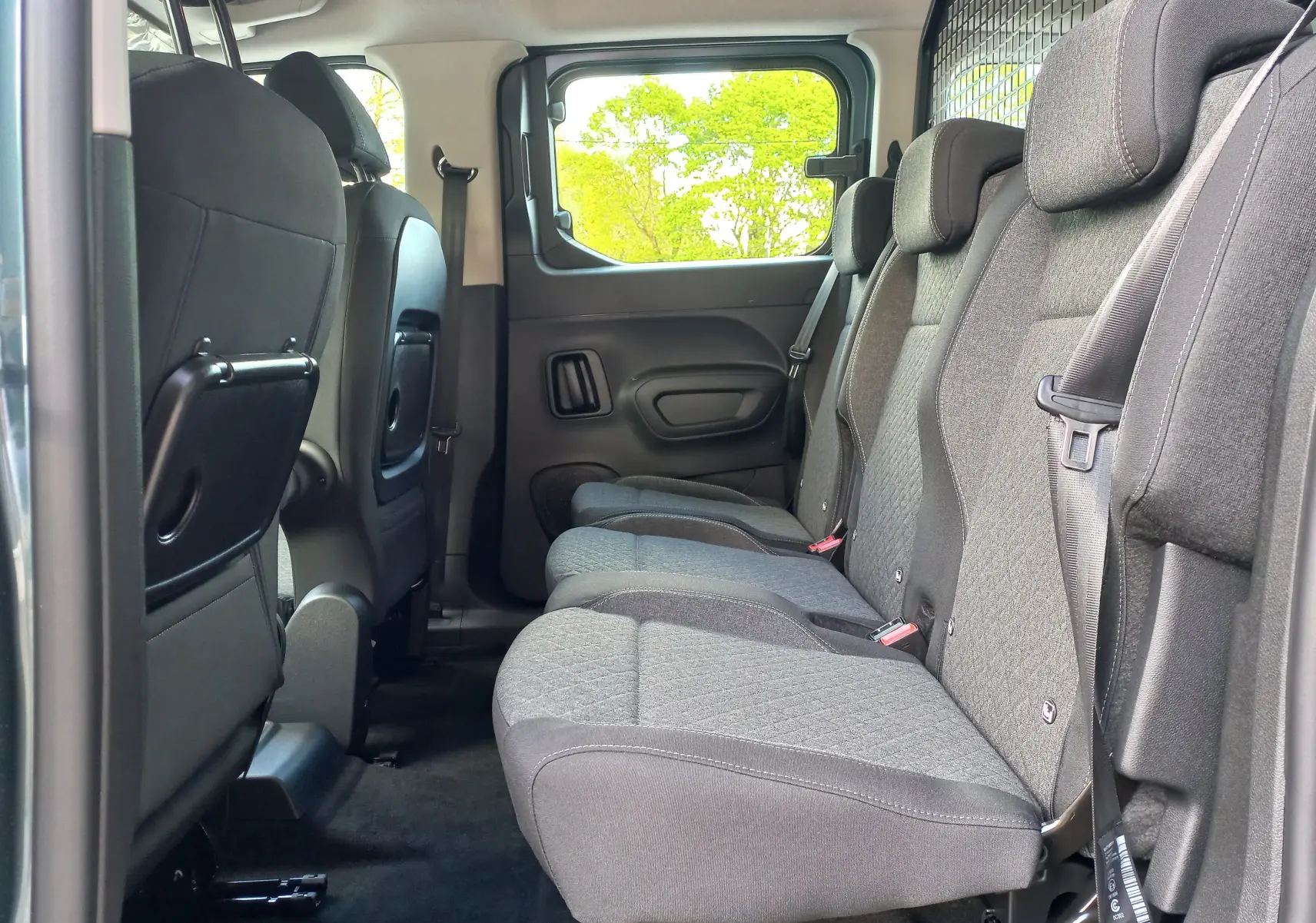 Vue intérieure côté droit des sièges arrière gris tissu de l’Opel Combo Life 2025, avec fenêtre et grille de séparation visibles.