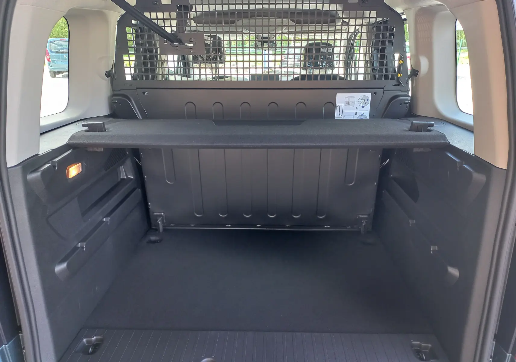 Vue intérieure arrière du coffre noir de l'Opel Combo Life bleu Kiama avec séparation grillagée et tablette rigide.