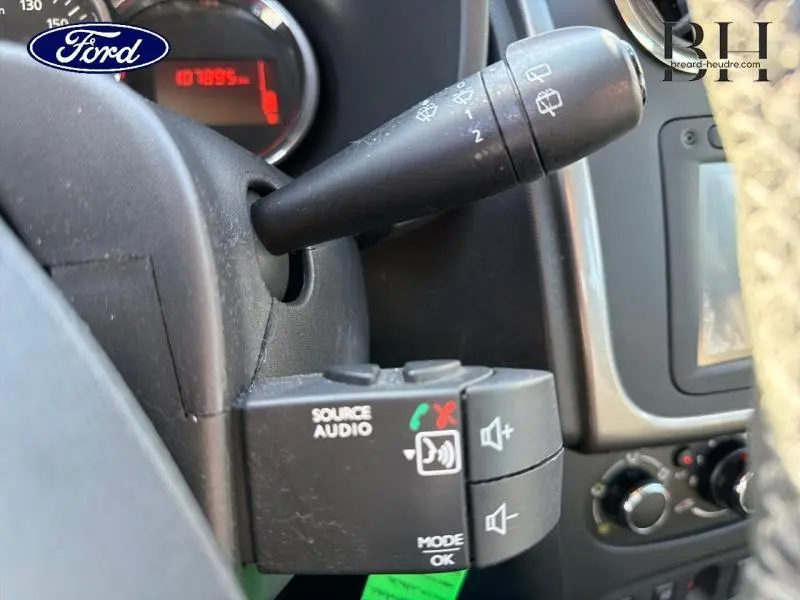 Gros plan sur la commande audio au volant et le commodo d’essuie-glace dans l’habitacle d’une Dacia Sandero noir nacré.