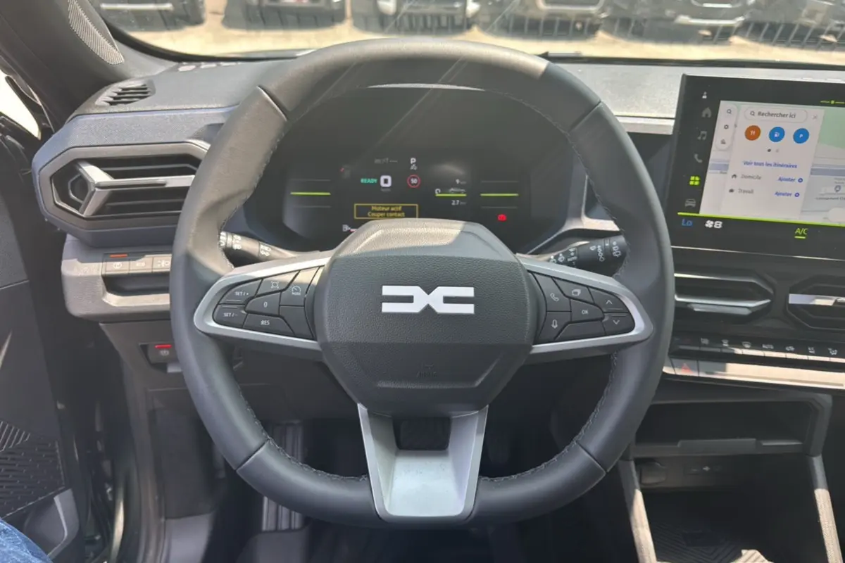 Vue intérieure centrée sur le volant cuir noir du Dacia Duster HEV 140 Journey Plus avec écran tactile et tableau de bord numérique.