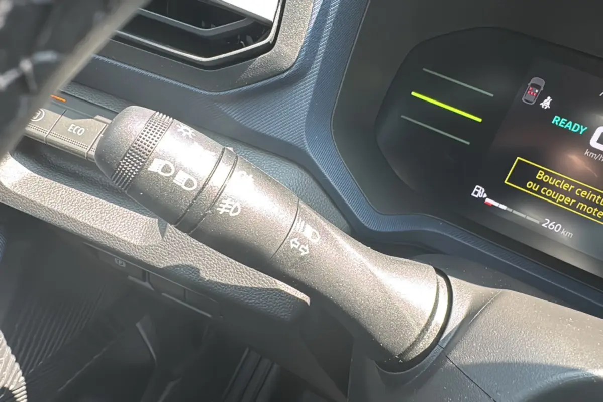 Gros plan sur la commande des feux à gauche du volant du tableau de bord d’un Dacia Duster vert cèdre 2025.