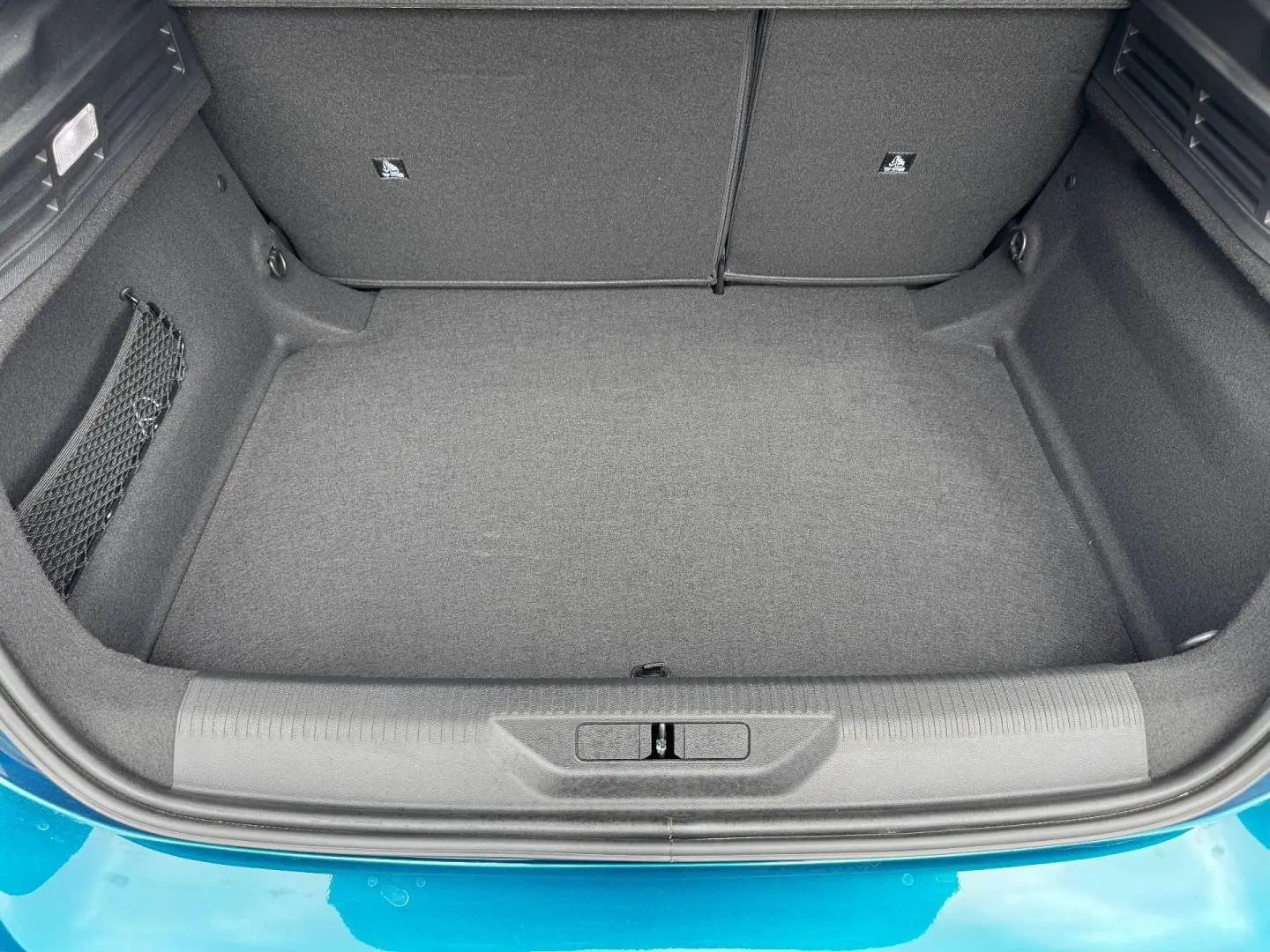 Coffre vide vu de dessus d'une Peugeot 308 1.2 Hybrid bleu, montrant la moquette et les rangements latéraux.