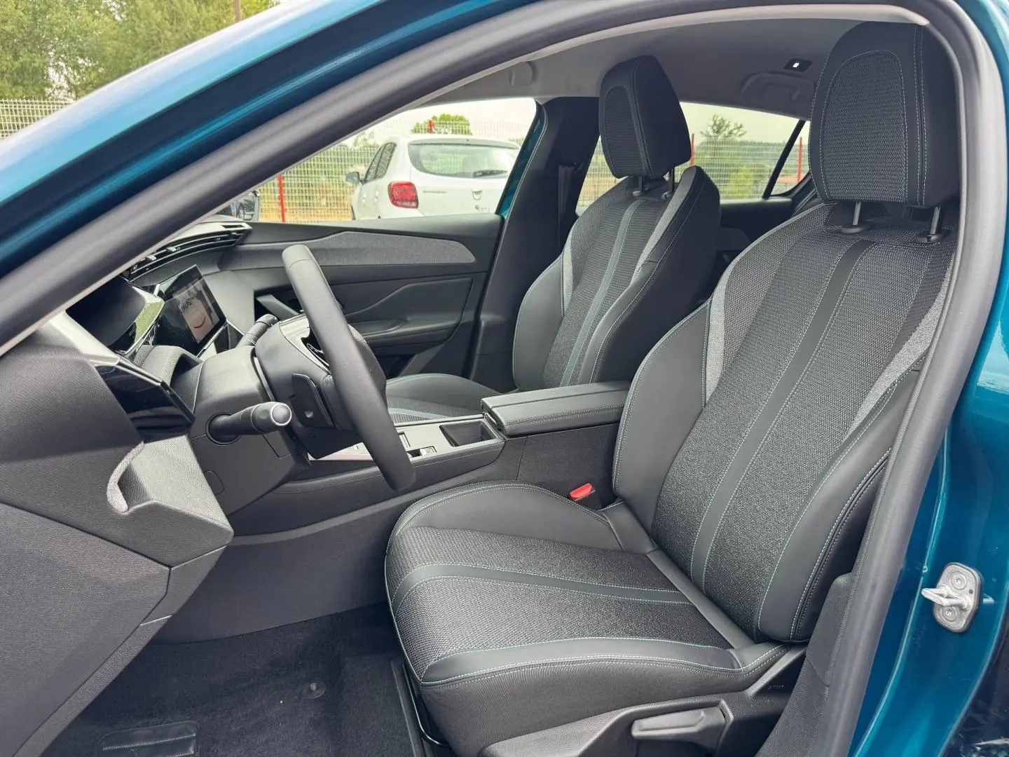 Vue intérieure côté conducteur de la Peugeot 308 bleu, sièges en tissu et cuir avec console centrale et volant multifonction.