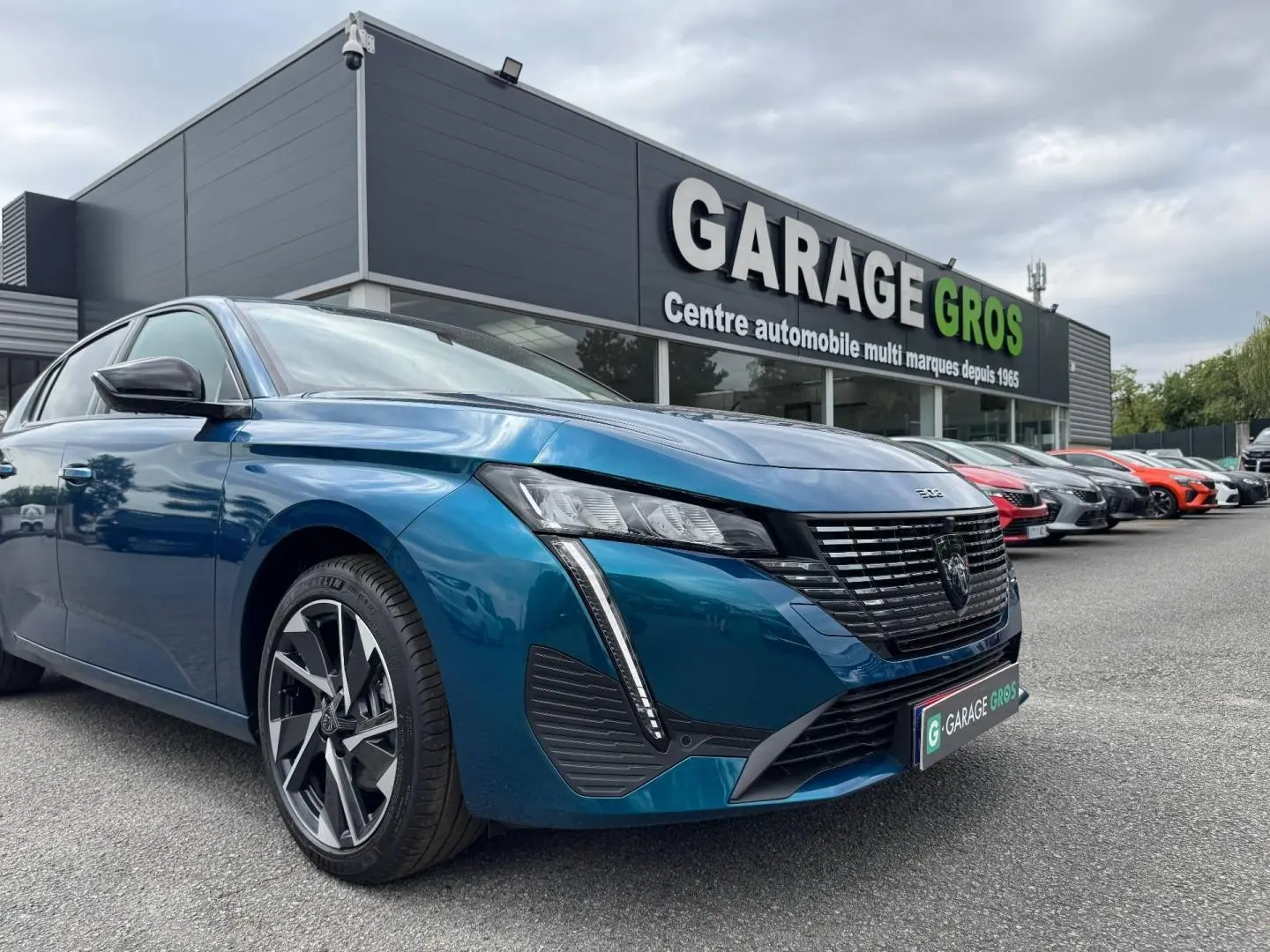PEUGEOT 308 bleu 3/4 avant droit avec calandre noire et feux LED, devant un garage automobile.