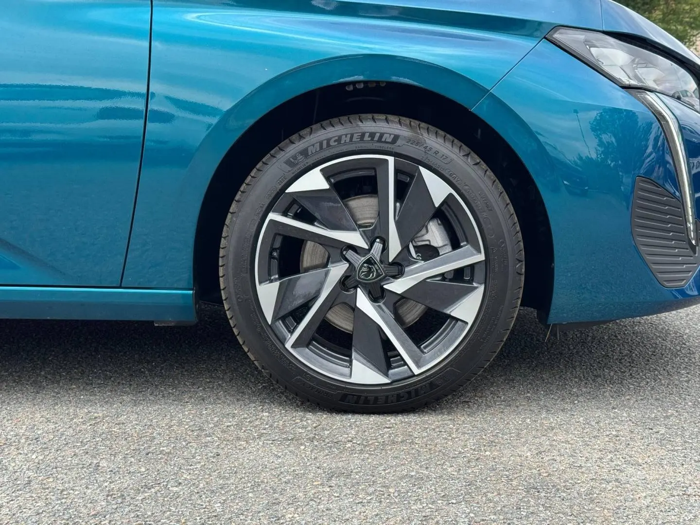 Gros plan sur la roue avant gauche et partie latérale d’une Peugeot 308 bleu Obsession avec jante alu stylisée.