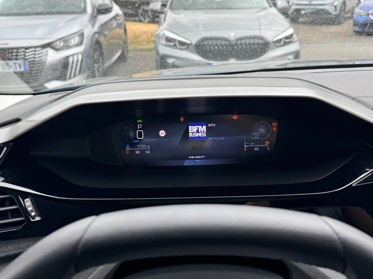 Vue intérieure du tableau de bord numérique de la Peugeot 308 bleu, affichant la radio BFM Business et les indicateurs de conduite.