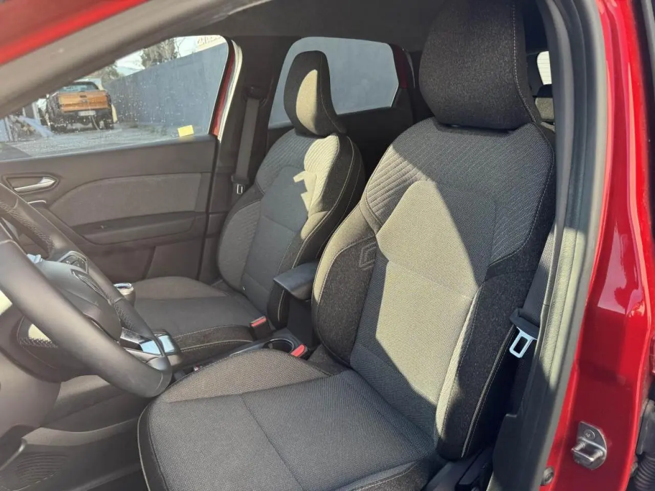 Vue intérieure côté conducteur du Renault Captur rouge flamme, sièges tissu gris avec accoudoir central.