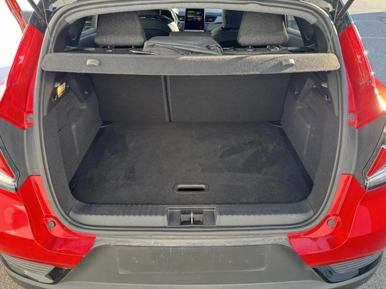 Coffre ouvert vu de l'arrière d'un Renault Captur rouge flamme avec intérieur noir et tablette cache-bagages.