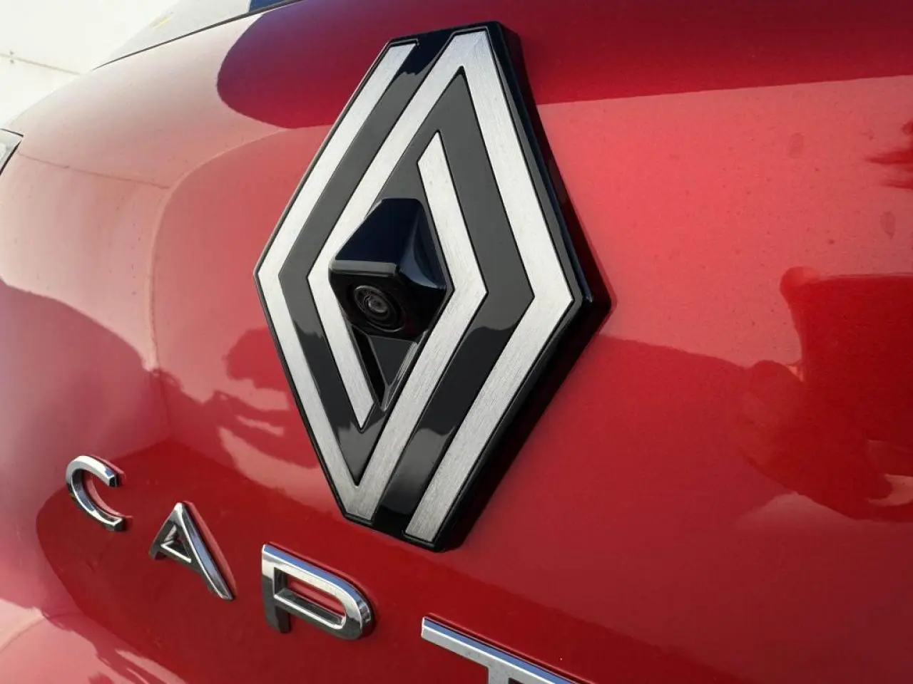 Gros plan sur le logo Renault avec caméra 360° intégrée sur la malle arrière rouge flamme du Captur II.