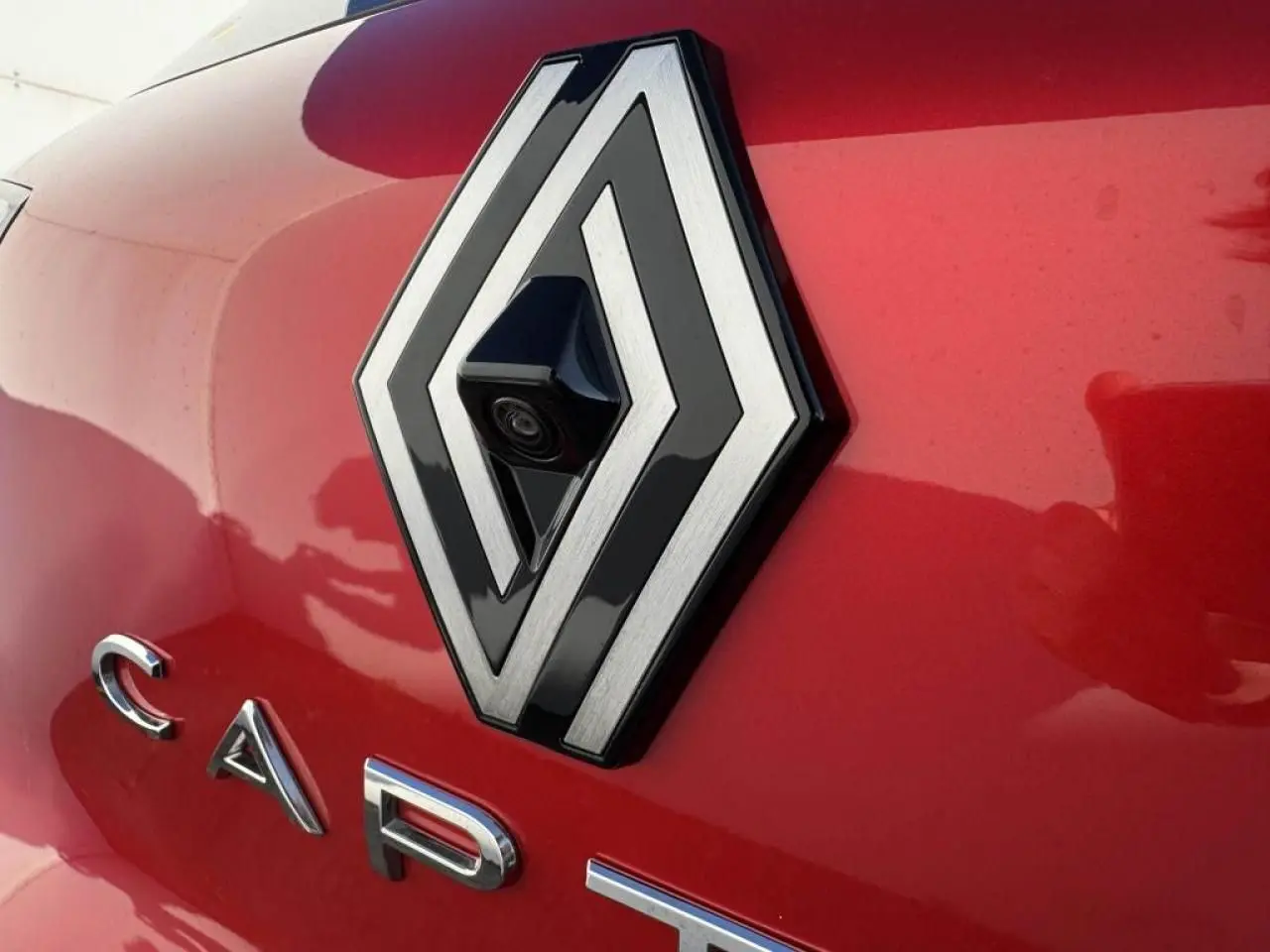 Gros plan sur le logo Renault rouge flamme avec caméra intégrée sur le hayon arrière du Captur II.