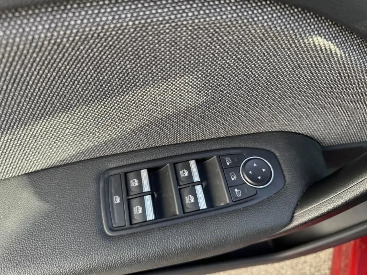 Gros plan sur les commandes des vitres électriques et rétroviseurs sur la porte côté conducteur du Renault Captur rouge flamme.