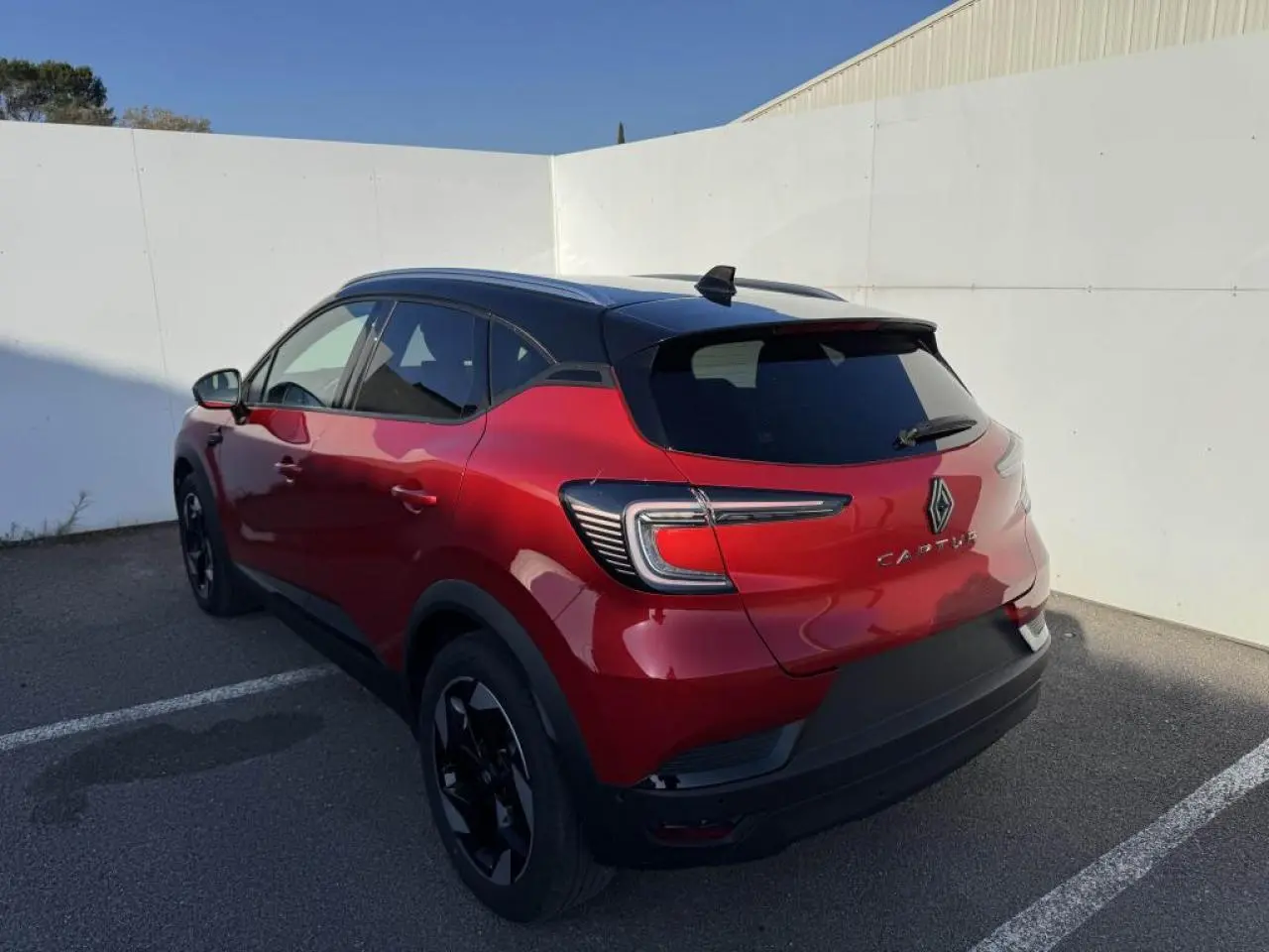 Vue 3/4 arrière droite du Renault Captur II rouge flamme avec toit noir et jantes noires dans un parking.