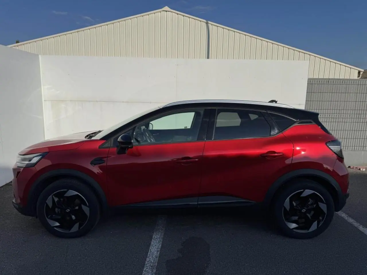 Profil droit d'un Renault Captur 2025 rouge flamme avec toit noir et jantes noires en aluminium.