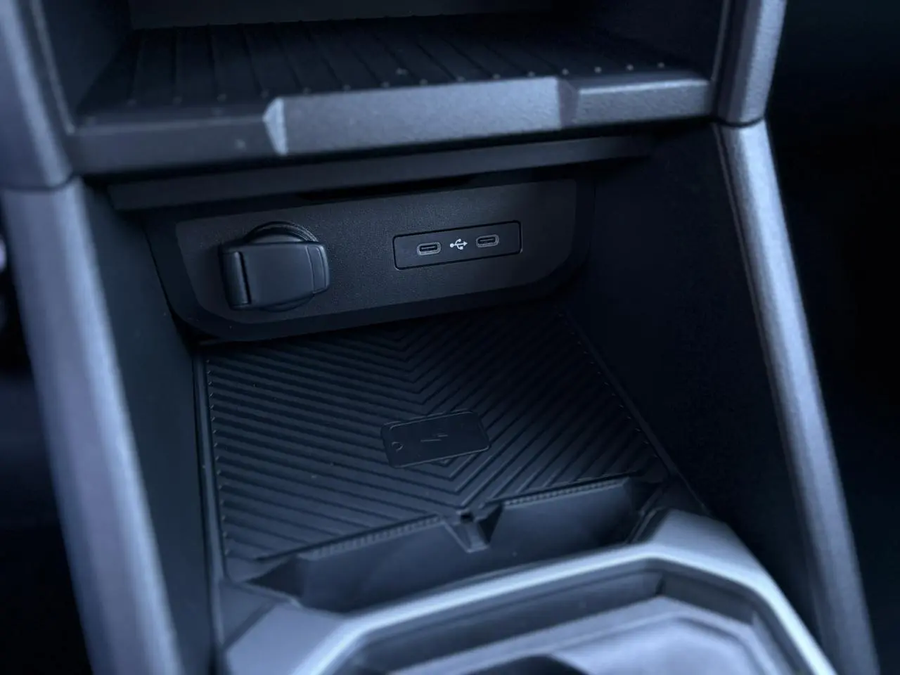 Gros plan sur la console centrale du Dacia Duster gris, montrant le chargeur à induction et ports USB-C.