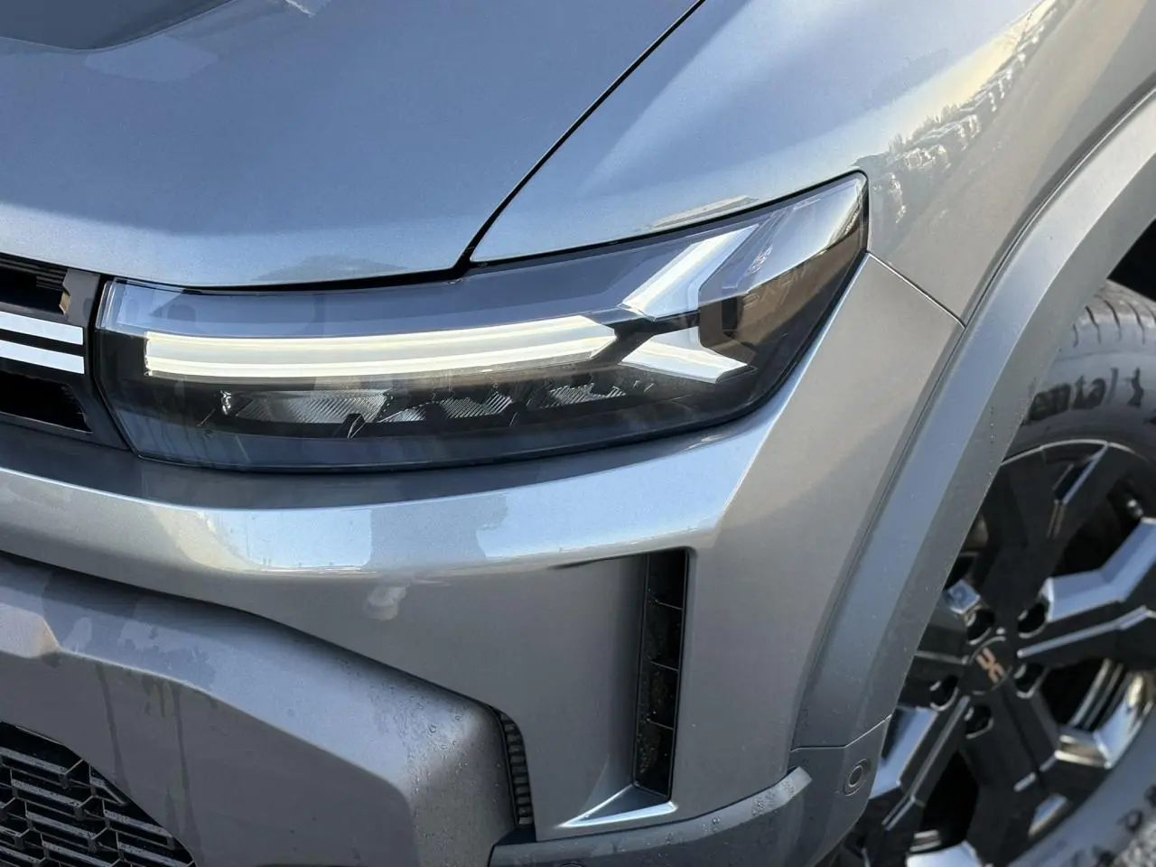 Gros plan sur l'avant droit du Dacia Duster gris schiste, mettant en valeur le phare LED et la jante alliage noire.