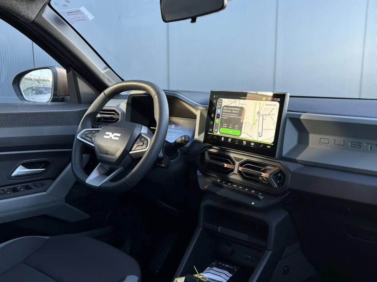 Intérieur du Dacia Duster 2025 gris, vue côté conducteur, tableau de bord avec écran tactile GPS et volant multifonction.