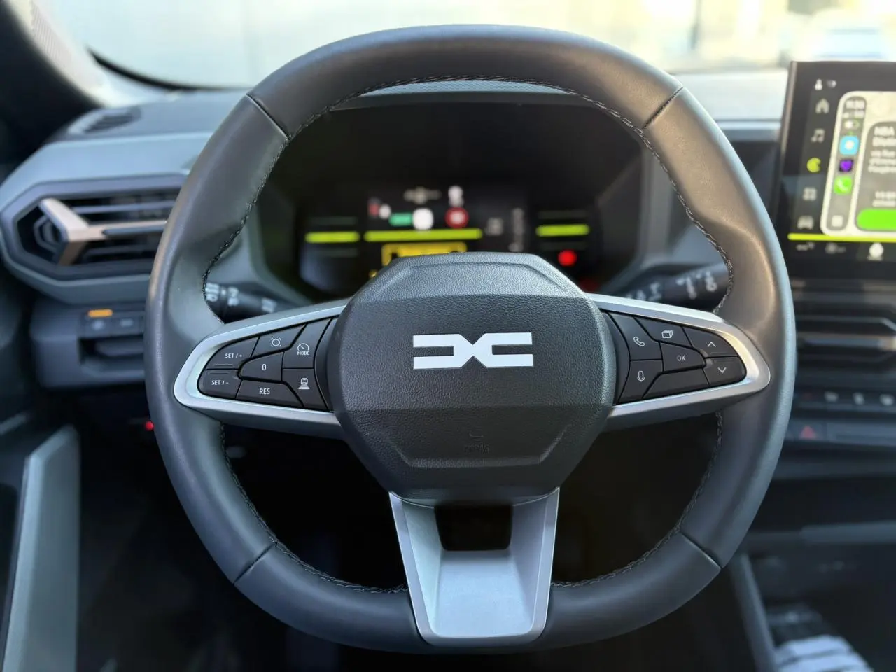 Vue rapprochée du volant noir du Dacia Duster 2025 avec commandes intégrées et tableau de bord digital en arrière-plan.