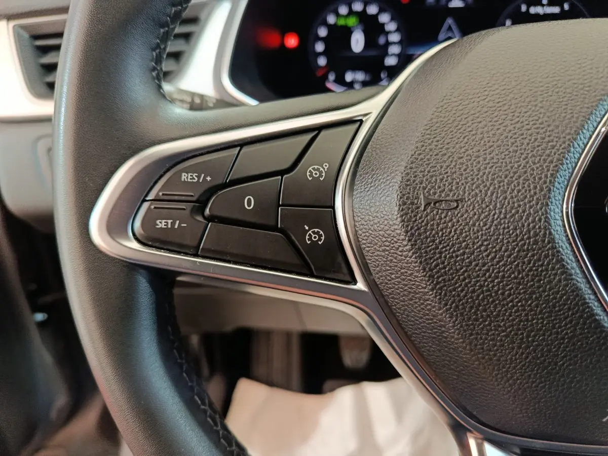 Gros plan sur les commandes du volant noir du Renault Captur Techno TCe 90 2024, avec affichage numérique flou en arrière-plan.