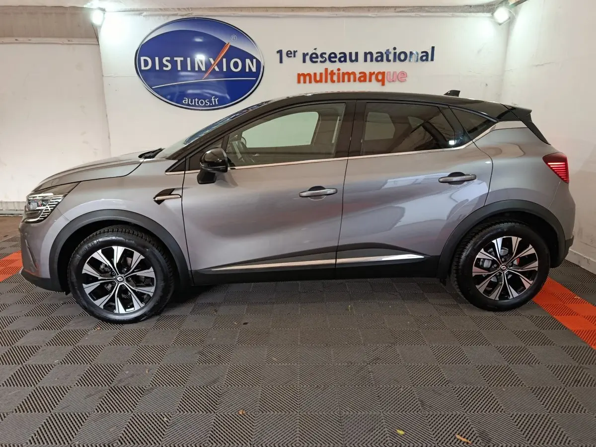 Profil côté gauche d'un Renault Captur Techno TCe 90 gris foncé 2024 avec jantes noires et toit noir contrasté.