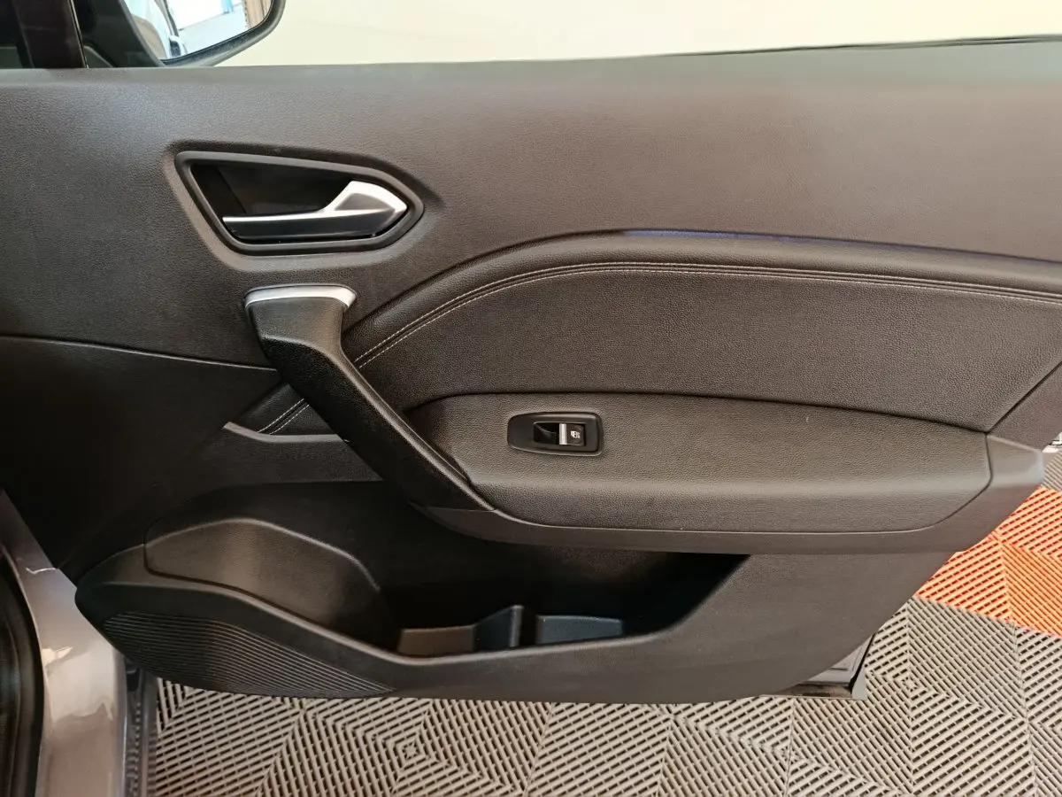 Porte intérieure côté gauche noire du Renault Captur 2024 techno TCe 90 avec poignée argentée et bouton de vitre électrique.