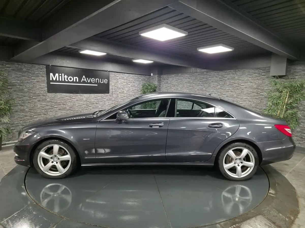 Profil côté gauche d'une Mercedes CLS 250 CDI gris métallisé avec jantes alliage 5 branches en intérieur showroom.