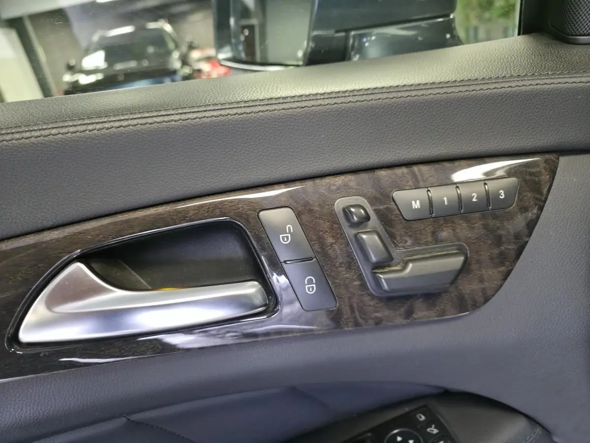 Gros plan sur la poignée intérieure et les commandes de réglage de siège en cuir gris avec insert bois d'une Mercedes CLS 250 CDI 2011.