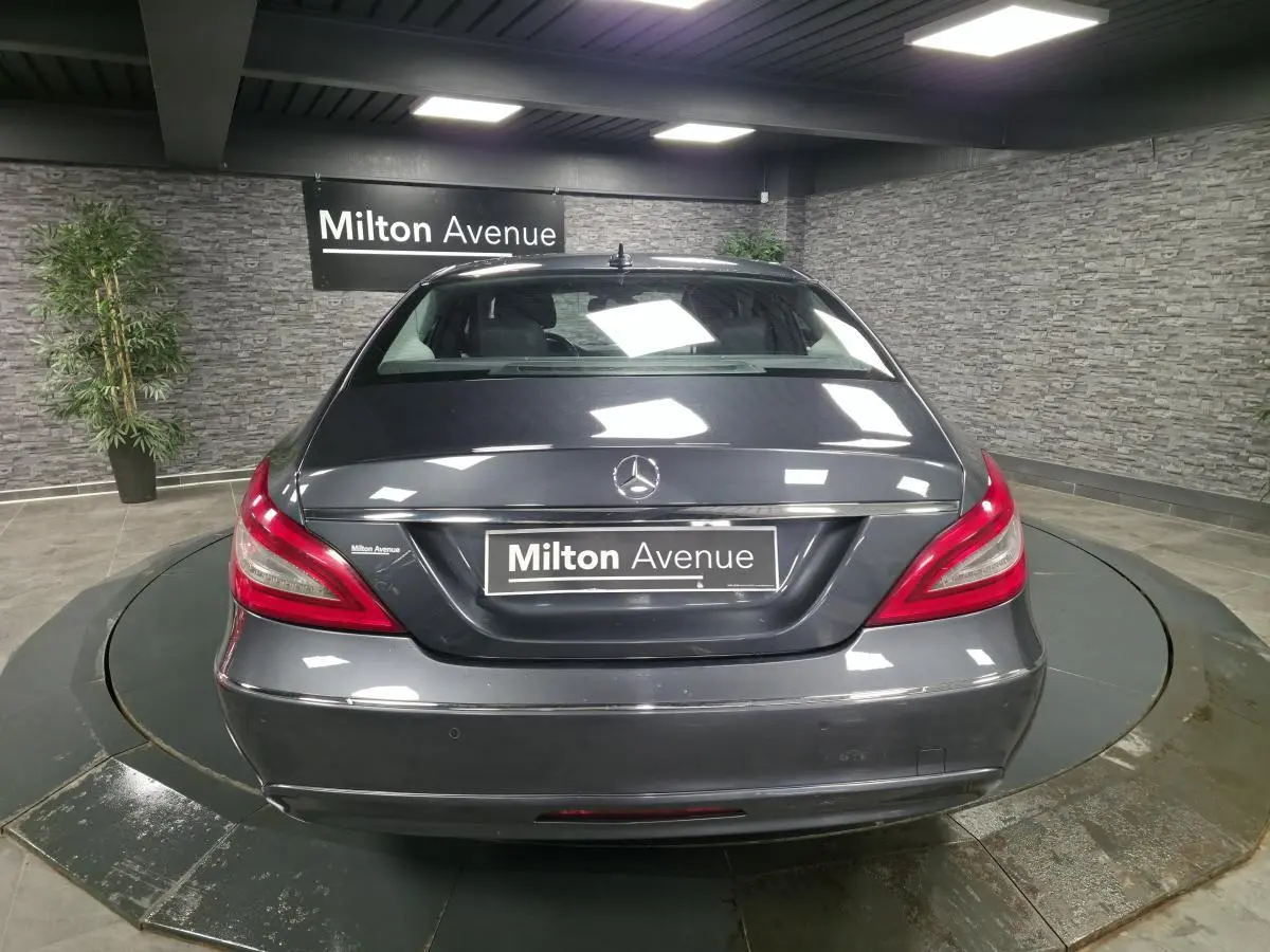 Vue arrière d'une Mercedes Classe CLS gris métallisé avec feux arrière rouges et plaque Milton Avenue dans un showroom.