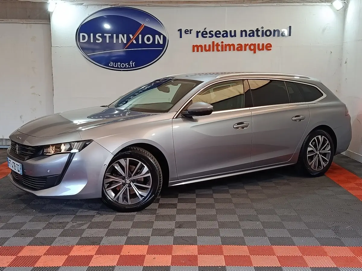Peugeot 508 break gris clair en 3/4 avant droit, avec jantes alliage et feux LED, stationné en intérieur showroom.