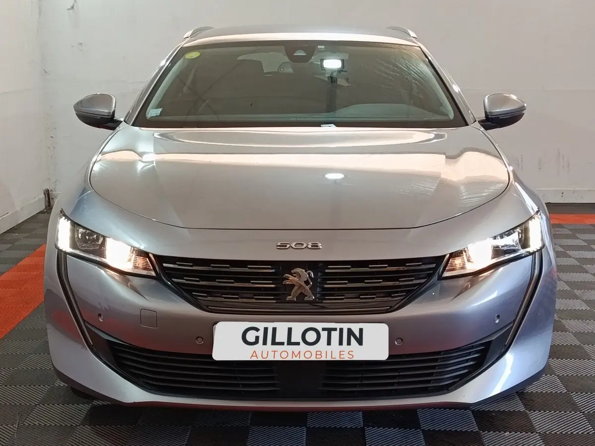 Vue frontale d'une Peugeot 508 gris clair avec phares allumés et calandre noire distinctive.