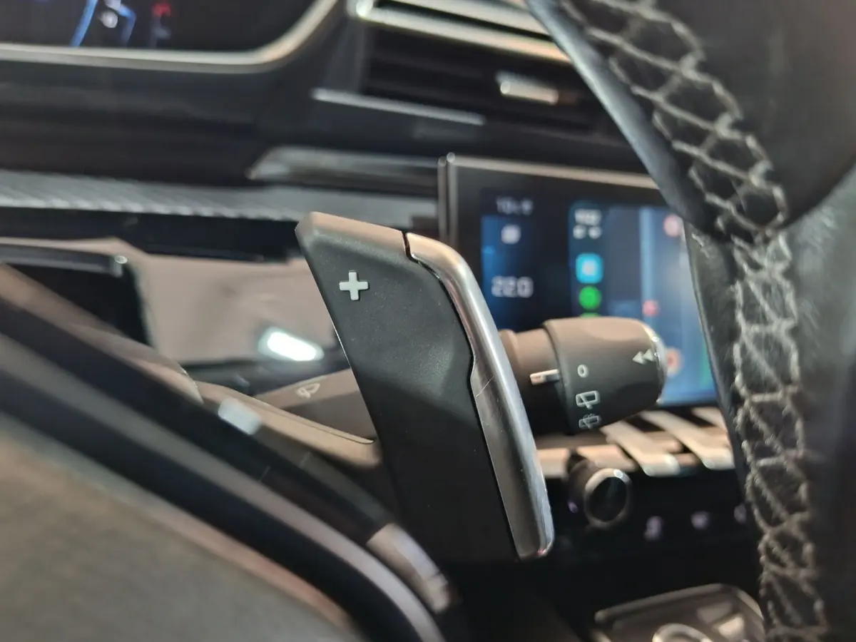 Gros plan sur la palette de changement de vitesse + côté droit du volant cuir de la Peugeot 508 gris clair, tableau de bord tactile en arrière-plan.