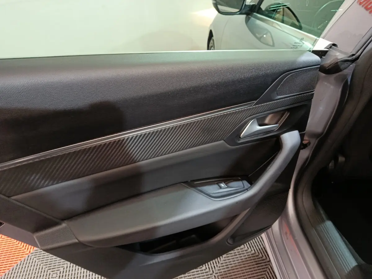 Vue intérieure côté gauche de la porte avant gris clair de la Peugeot 508 avec insert effet carbone et poignée argentée.