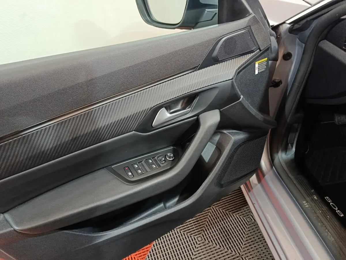 Vue intérieure du panneau de porte côté conducteur gris clair de la Peugeot 508 avec commandes électriques et finition carbone.