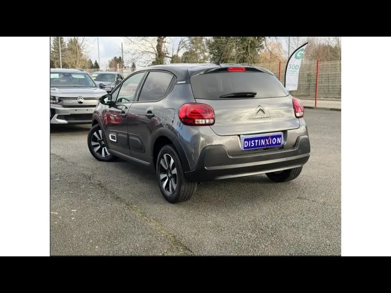 Vue 3/4 arrière droite d'une Citroën C3 2023 gris Platinium avec toit noir et feux arrière rouges, stationnée sur parking extérieur.