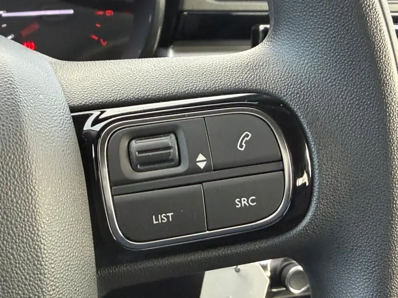 Gros plan sur les commandes du volant côté gauche d'une Citroën C3 2023, finition Gris Platinium et Noir Perla Nera.