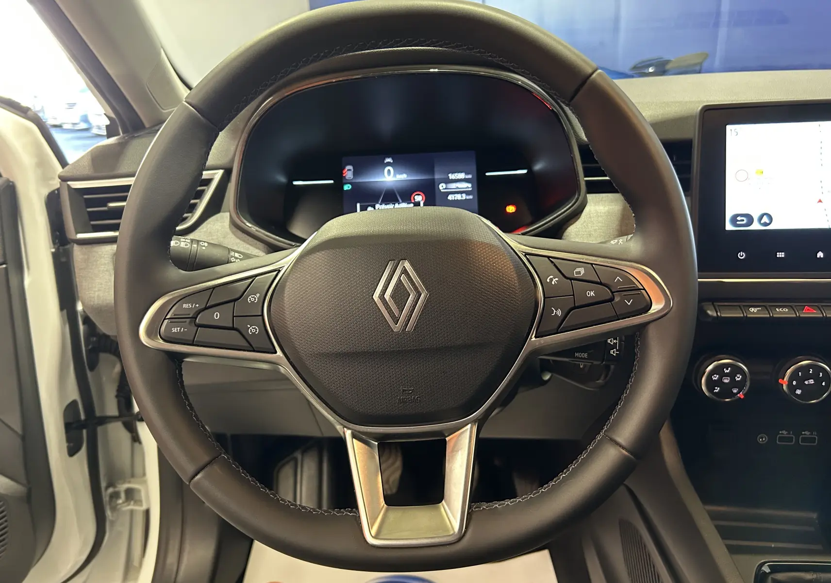 Vue intérieure centrée sur le volant cuir noir de la Renault Clio V, avec tableau de bord numérique et écran tactile GPS visible.