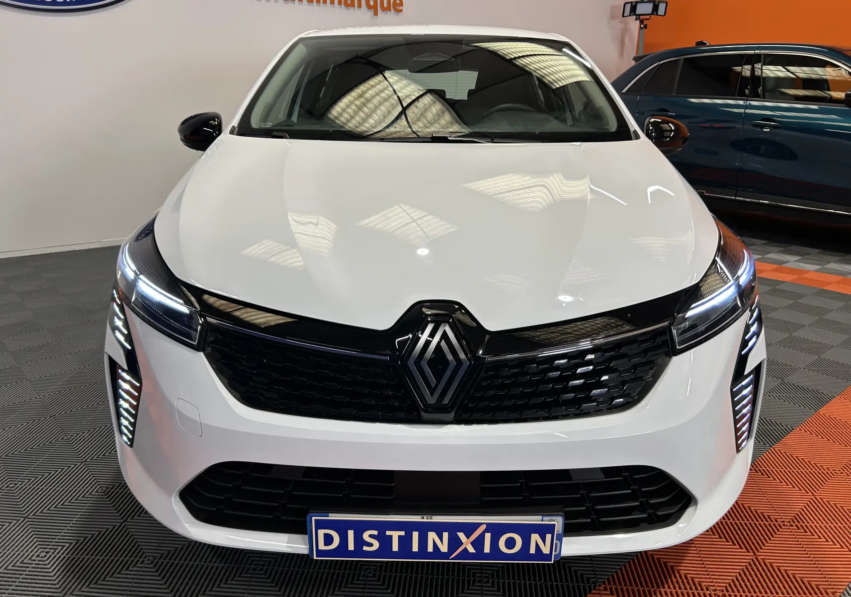 Vue de face d'une Renault Clio V blanche avec calandre noire et feux LED allumés dans un showroom.