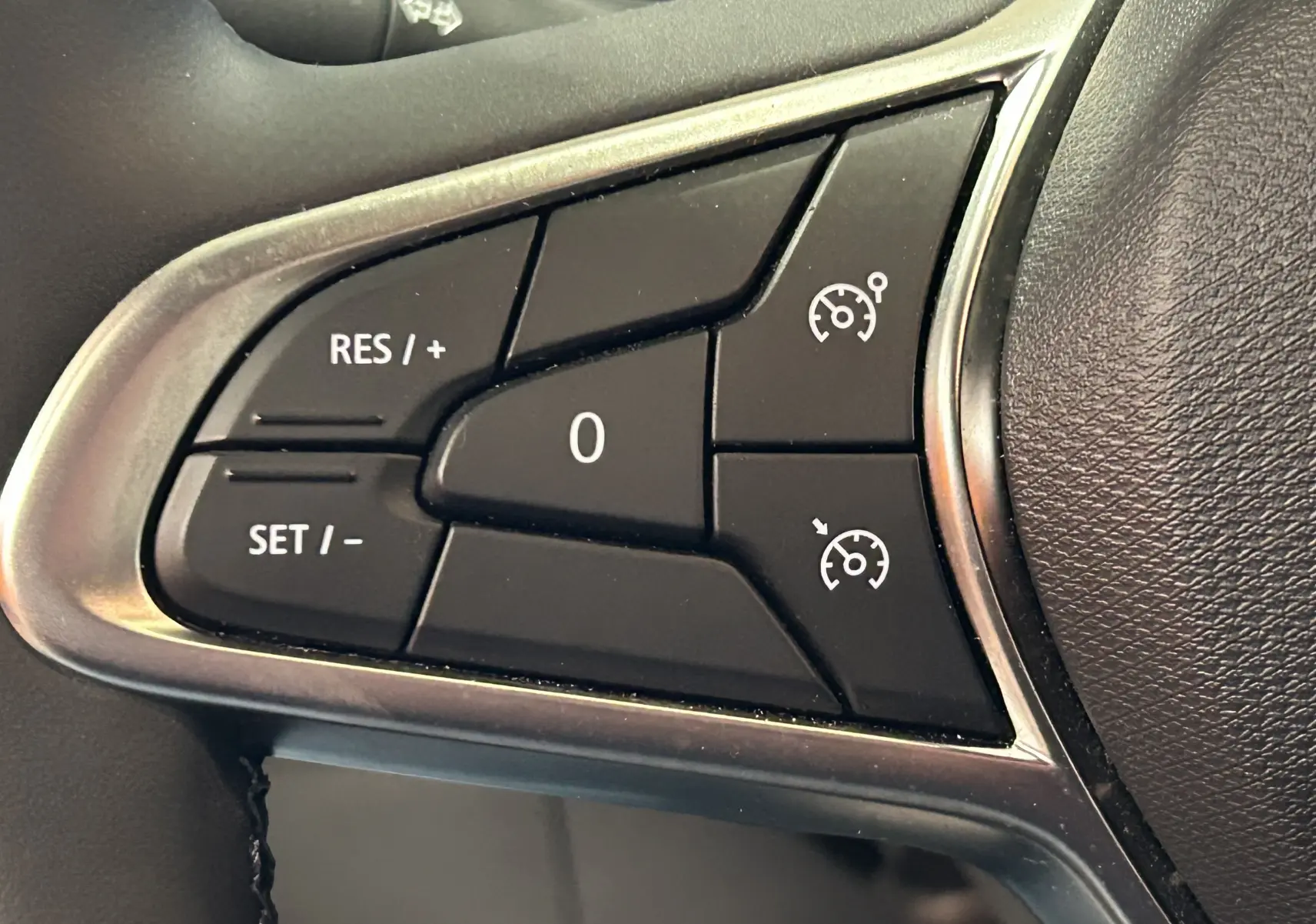 Gros plan sur les commandes de régulateur de vitesse au volant d'une Renault Clio V blanche, version BlueDCI 100 Evolution.