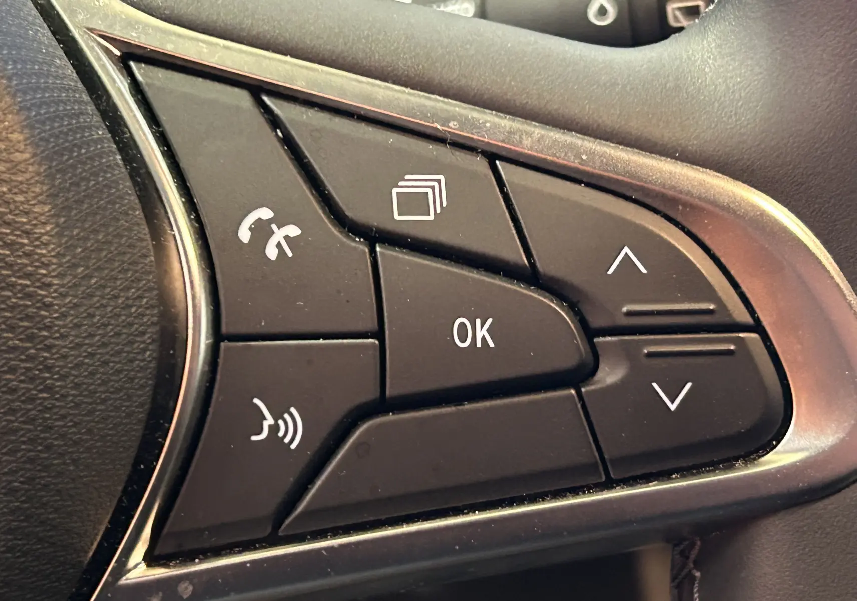 Gros plan sur les commandes multifonctions noires du volant côté gauche d’une Renault Clio V blanche.