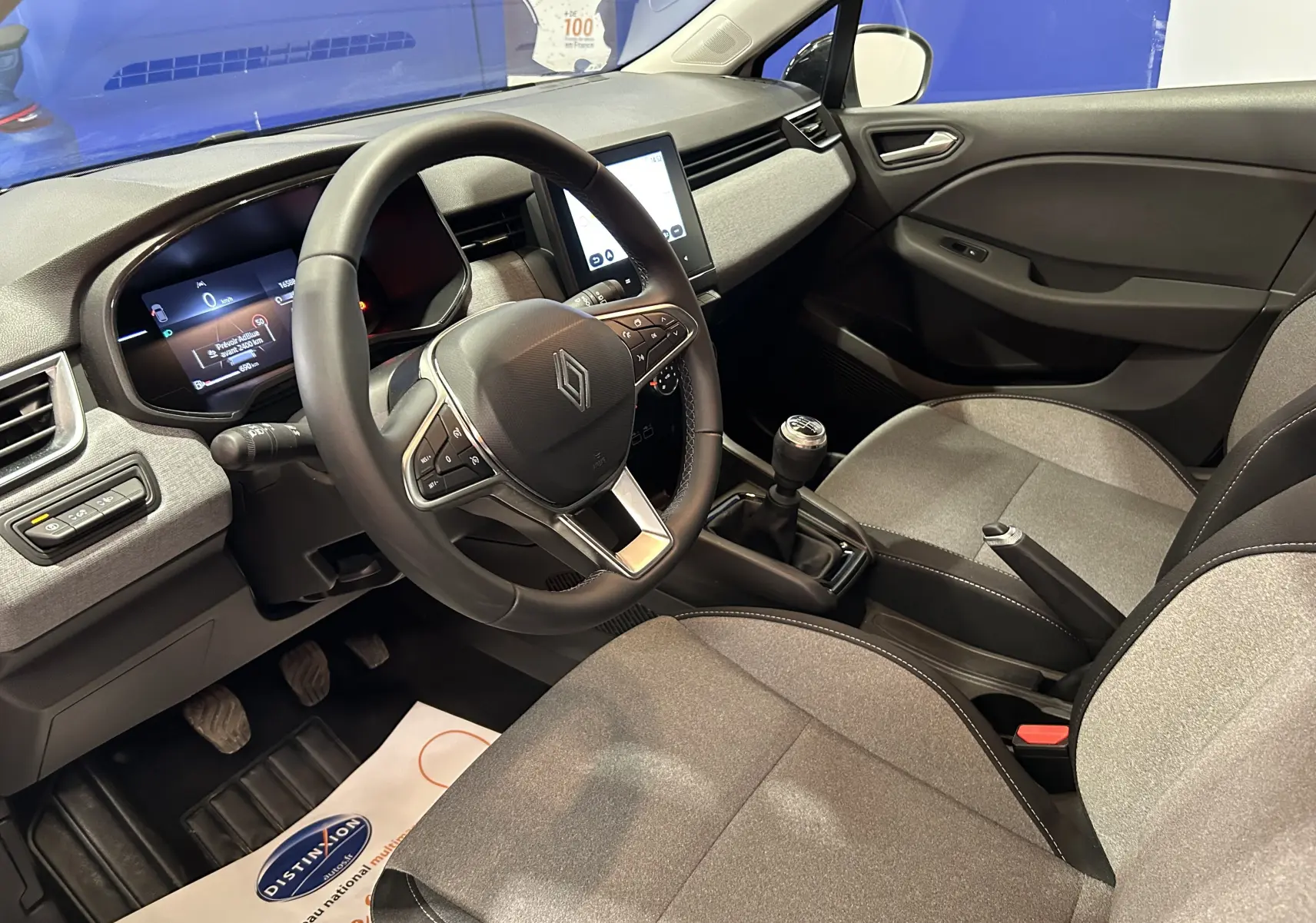 Intérieur de la Renault Clio V blanche, vue côté conducteur, volant multifonction et boîte manuelle visibles.