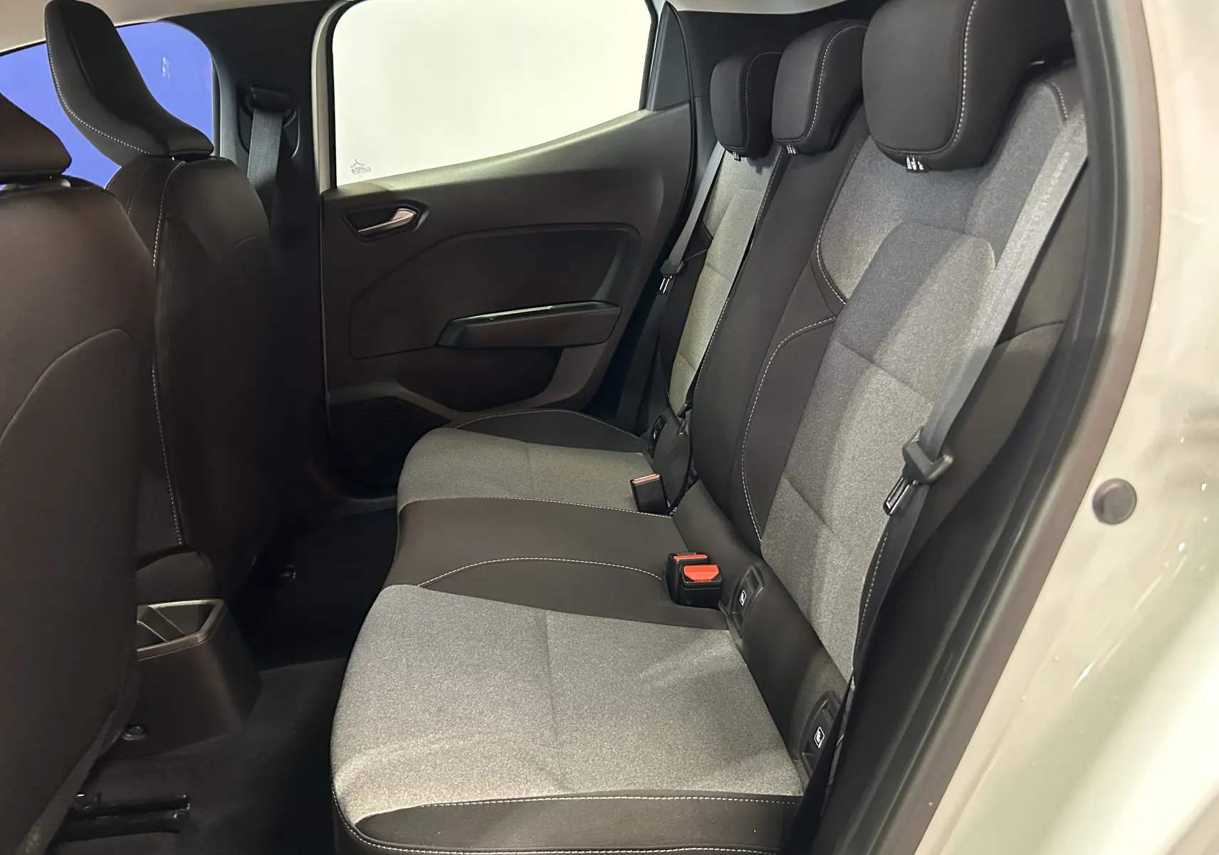 Vue latérale droite de l'intérieur arrière de la Renault Clio V blanc, sièges tissu gris et noir avec ceintures visibles.