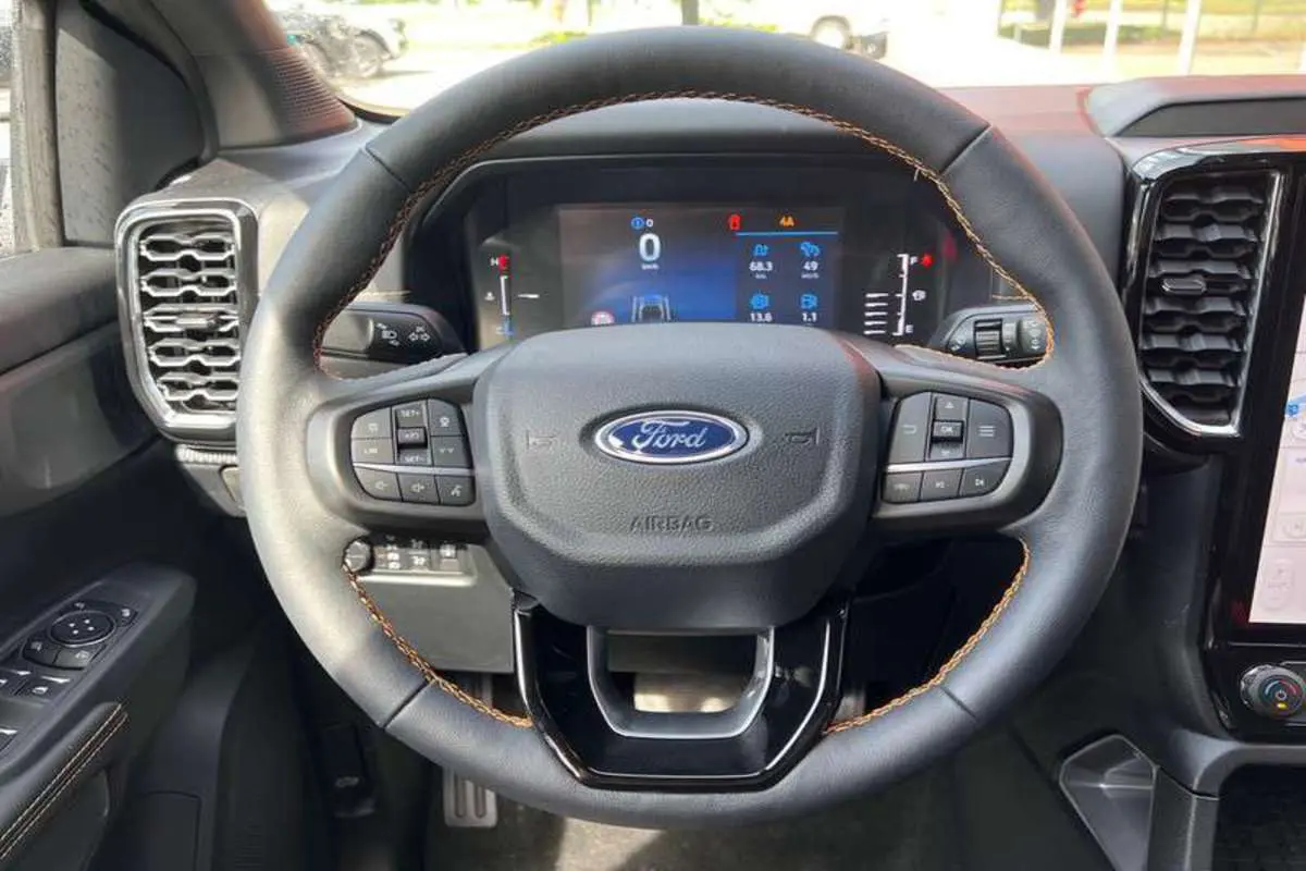 Vue rapprochée du volant cuir noir avec surpiqûres marron du Ford Ranger 2025, tableau de bord numérique visible.