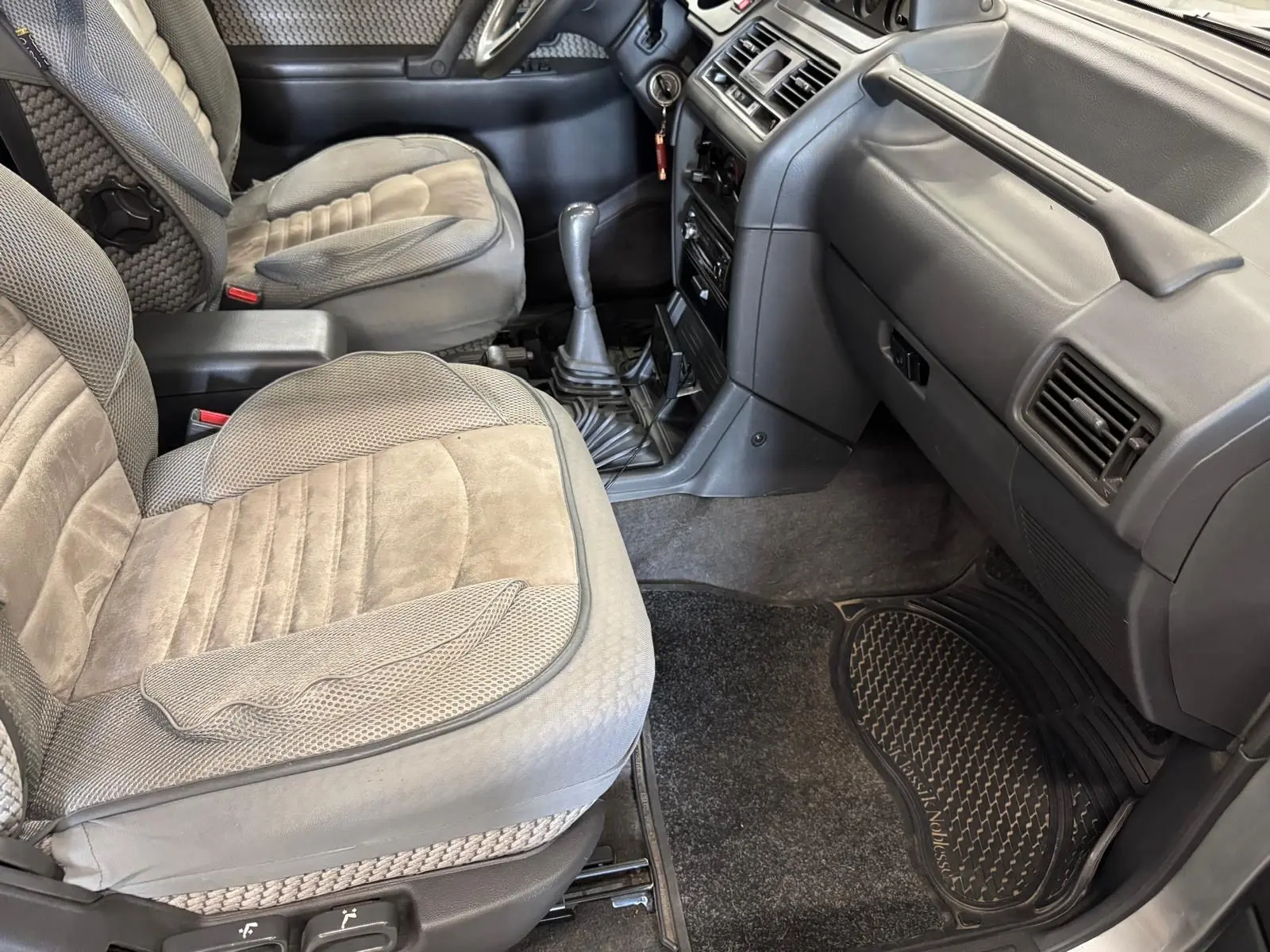 Vue intérieure côté passager du Mitsubishi Pajero Court 2.8 TD 1997 avec sièges gris et tapis en caoutchouc.