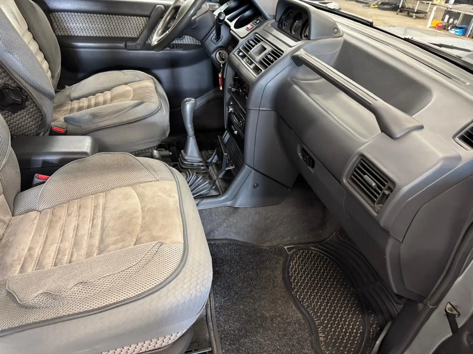 Vue intérieure côté passager du Mitsubishi Pajero Court 2.8 TD 1997 avec sièges gris et tableau de bord gris foncé.