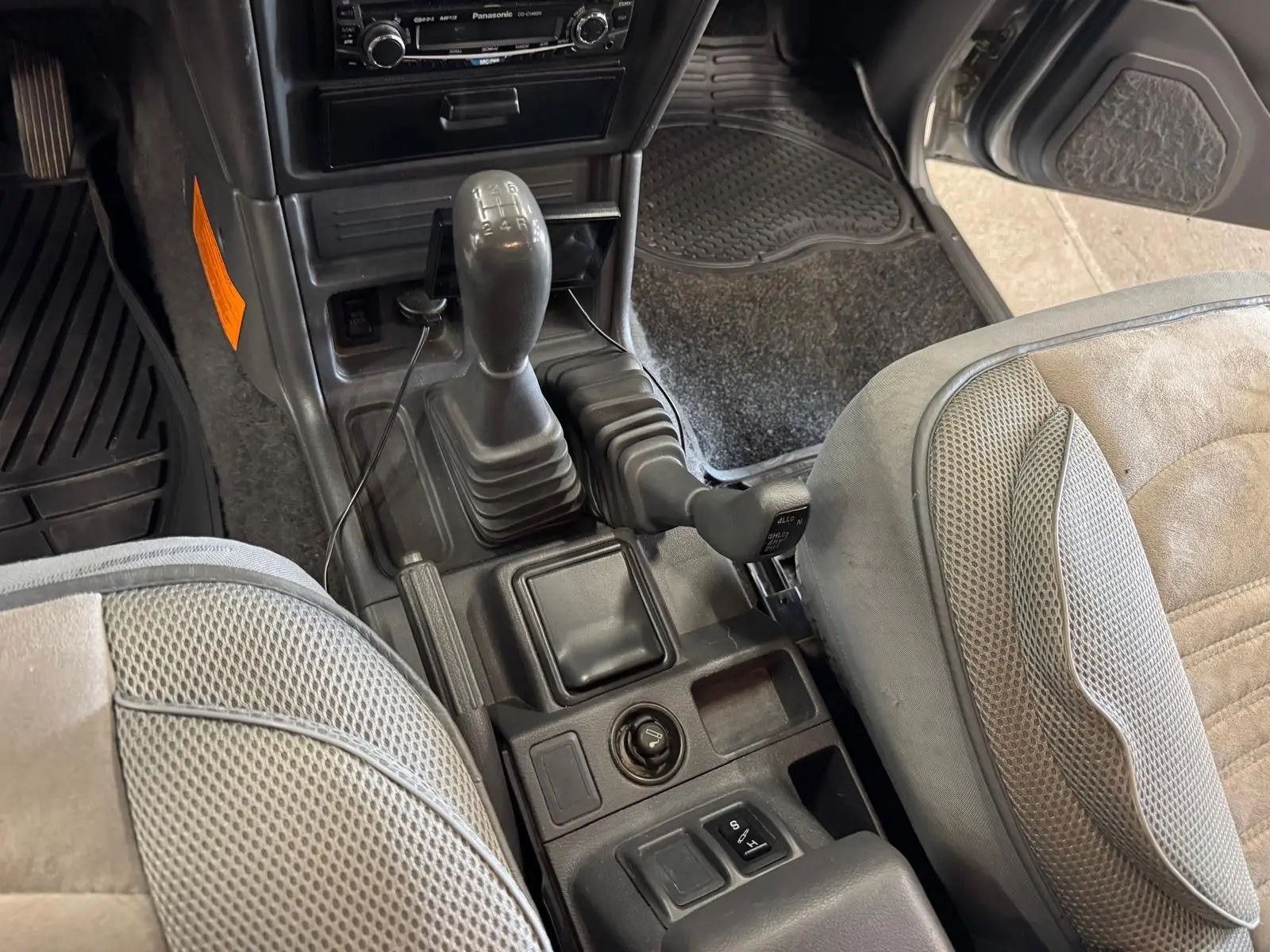 Vue intérieure centrée sur la console centrale et levier de vitesses d’un Mitsubishi Pajero Court gris aluminium de 1997.