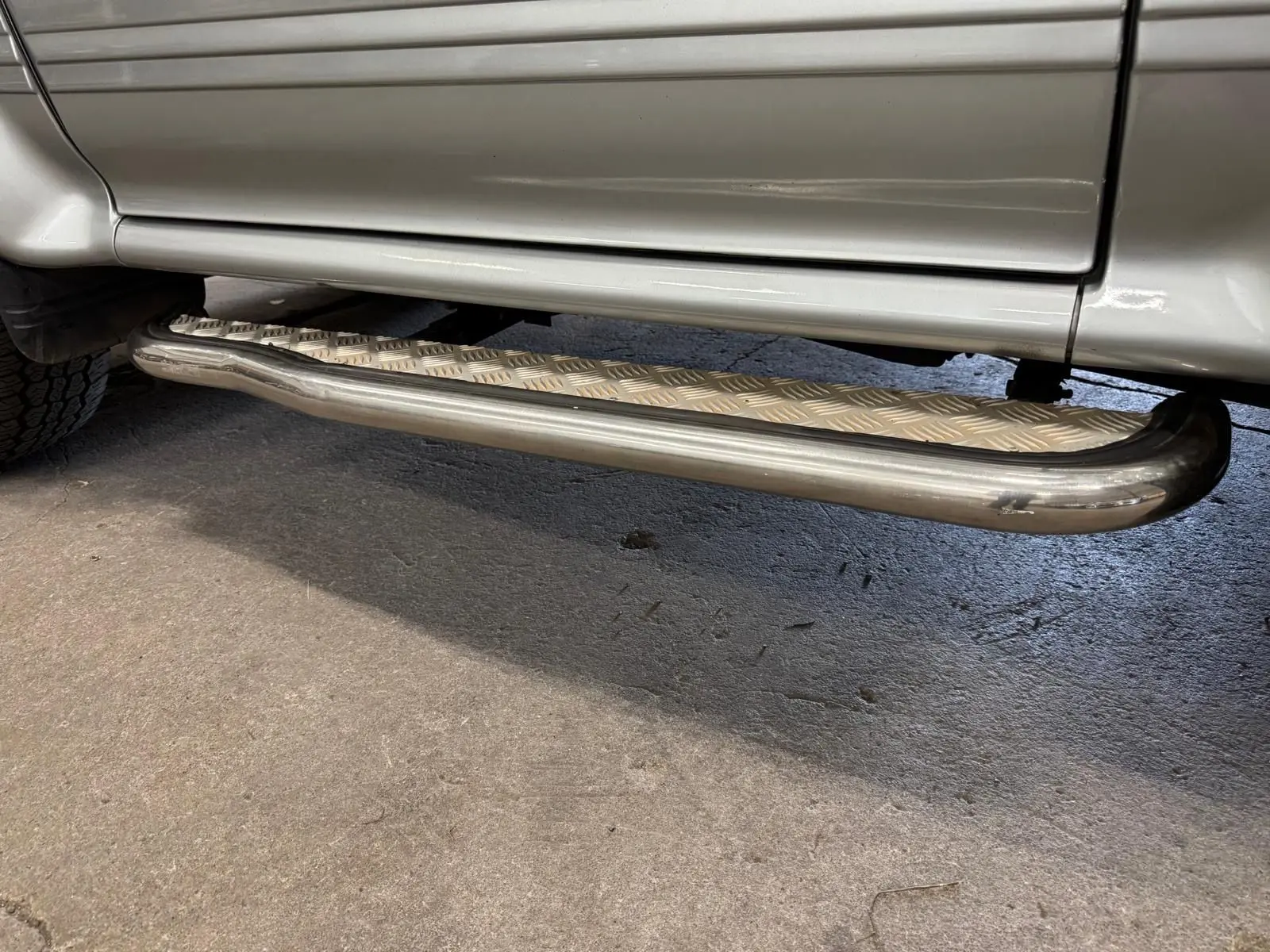 Gros plan sur le marchepied en métal strié sous la porte côté gauche du Mitsubishi Pajero Court gris aluminium.