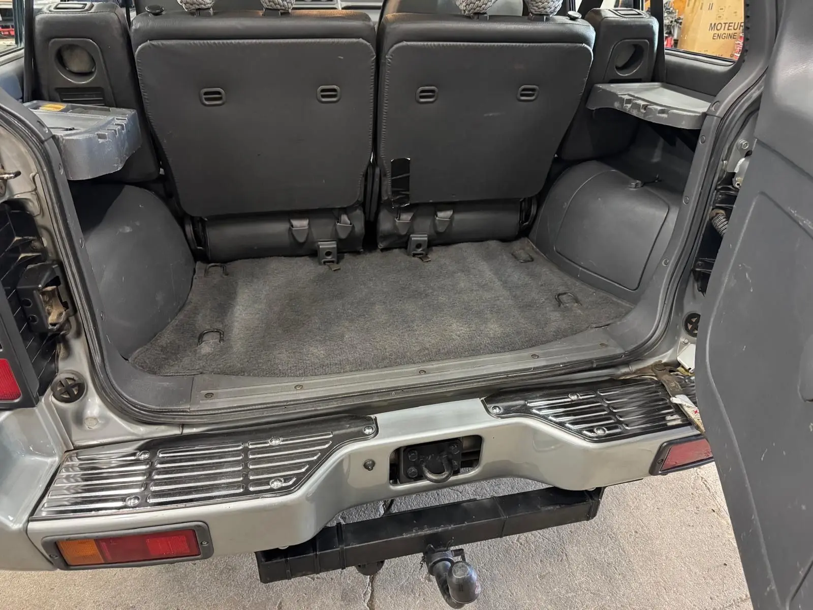 Vue arrière ouverte du Mitsubishi Pajero Court gris aluminium de 1997, montrant l'espace de coffre et l'attelage.