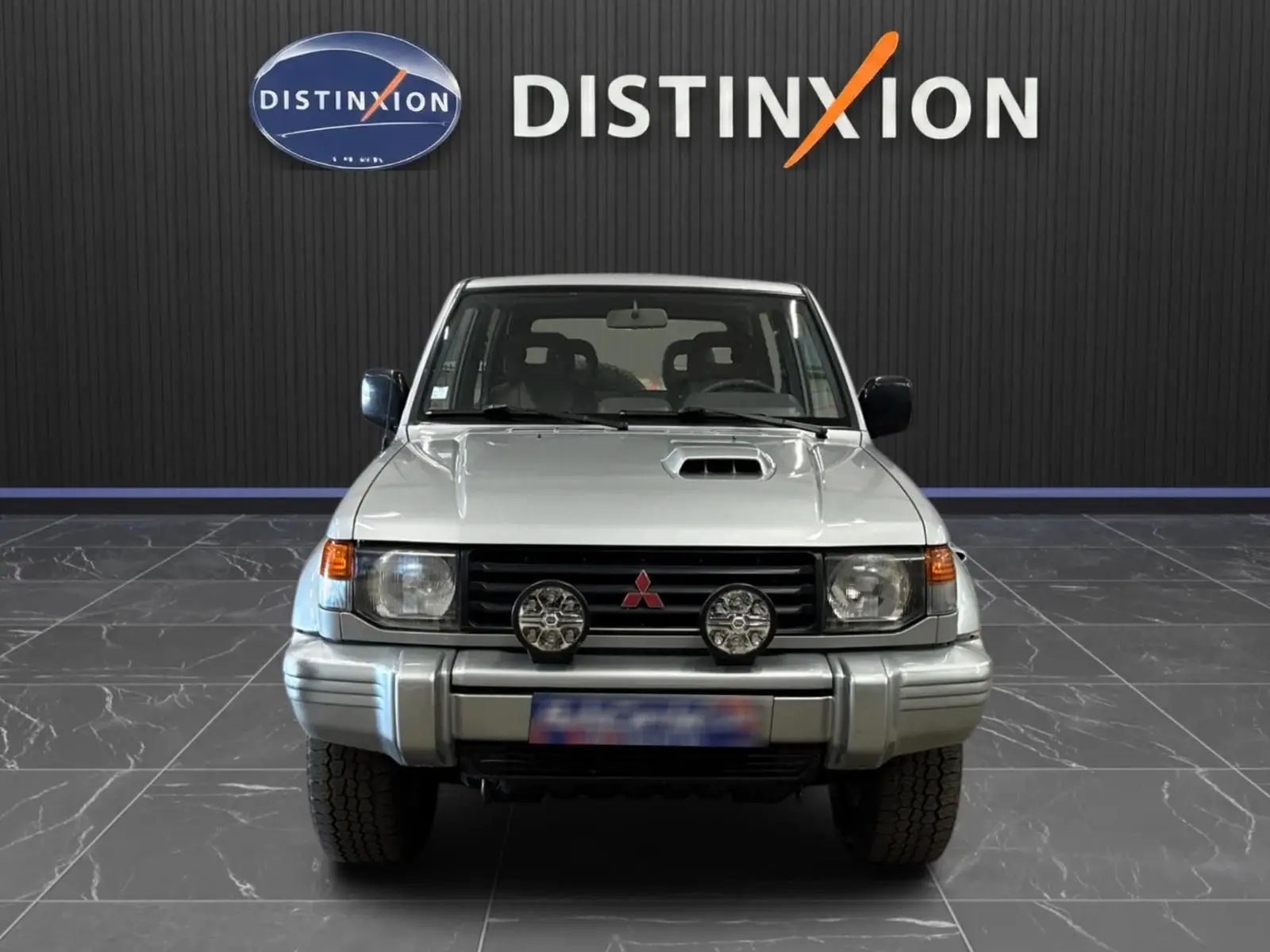 Vue de face du Mitsubishi Pajero Court gris aluminium de 1997 avec phares additionnels et prise d'air sur le capot.