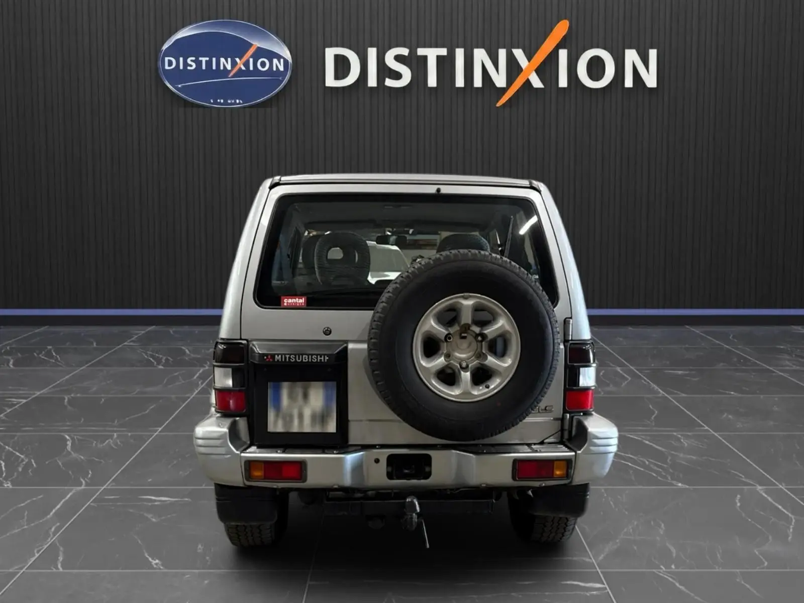 Vue arrière d'un Mitsubishi Pajero Court gris aluminium de 1997 avec roue de secours et attelage visible.